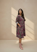 Woman wearing a knee-length loose floral dress in shades of mauve and rose, styled with rolled-up sleeves and pink heeled ankle boots, posing sideways in soft natural light.