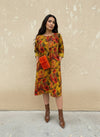Front view of woman in a yellow and red floral knee-length dress with pockets and cuffed sleeves, styled with a bold orange fuzzy bag and brown ankle boots.