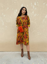 Front view of woman in a yellow and red floral knee-length dress with pockets and cuffed sleeves, styled with a bold orange fuzzy bag and brown ankle boots.