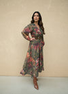 Woman wearing a green floral wrap maxi dress with red and gold floral prints, styled with a wide brown belt and brown ankle boots.