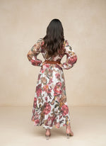 Woman wearing a long-sleeve floral maxi dress with a brown belt, viewed from the back, showing flowing fabric with red and pink flower patterns.