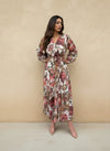 Woman posing in a white floral wrap maxi dress with pink and brown flower prints, styled with a tie waist and blush pink ankle boots.
