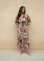 Woman posing in a white floral wrap maxi dress with pink and brown flower prints, styled with a tie waist and blush pink ankle boots.