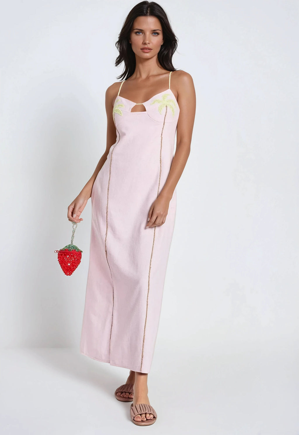 Model wearing a light pink midi dress with palm tree embroidery and a front cut-out, holding a red beaded strawberry bag.