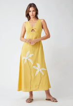Model wearing sleeveless yellow cotton dress with front cutout and white palm tree embroidery near the hem, posing against a light grey background.
