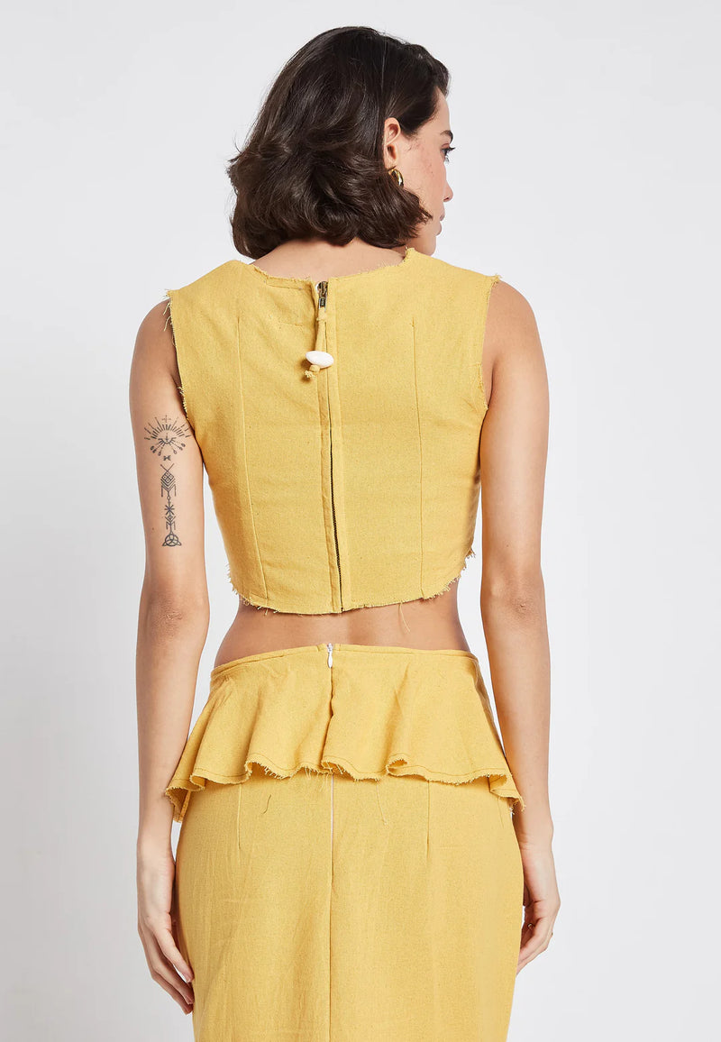  Back view of the golden yellow crop top featuring a visible zipper and decorative shell charm, paired with a matching skirt that has a subtle ruffle detail at the waistband.