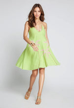 Woman wearing a sleeveless lime green cotton mini dress with a halter neckline and light pink palm tree embroidery. The dress has a relaxed A-line silhouette and frayed hem.