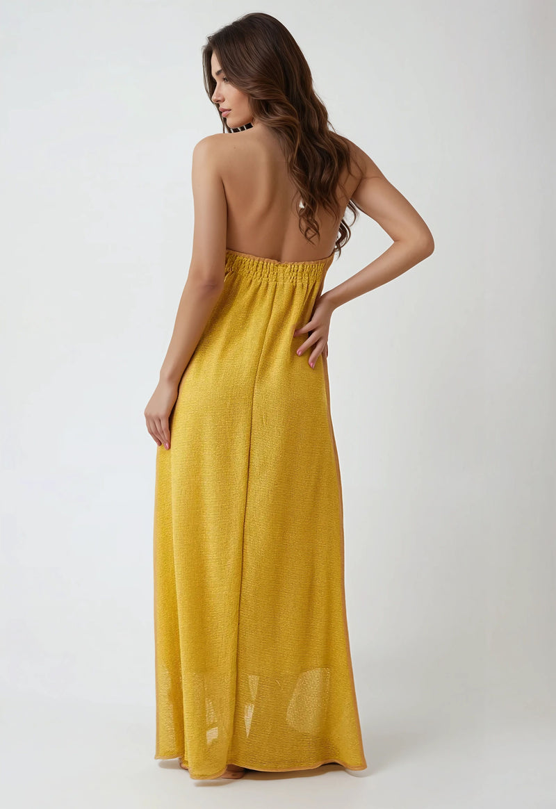 Back view of a woman wearing a mustard yellow strapless-style halter maxi dress with an elasticized back.