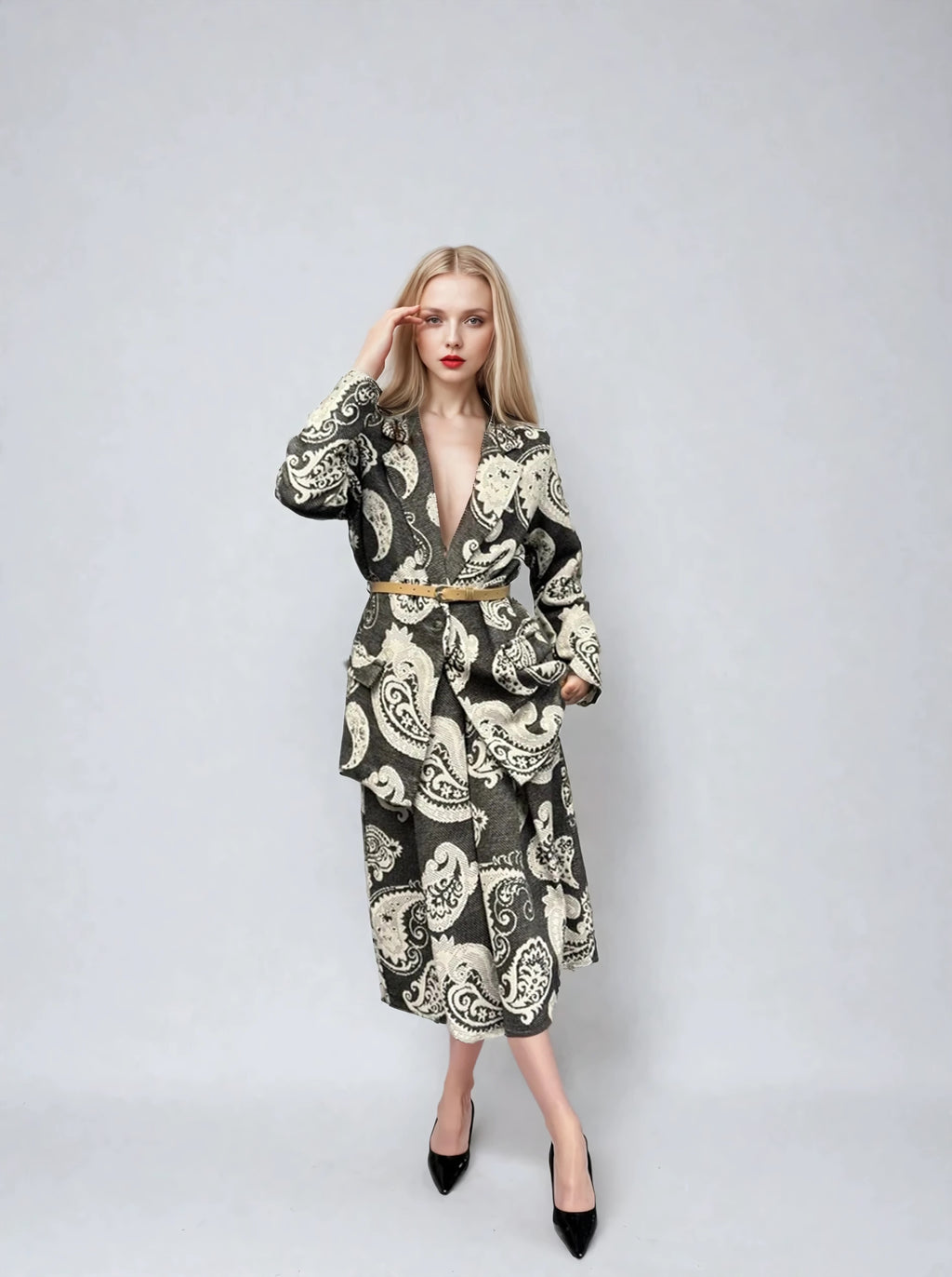 Woman wearing a statement paisley-patterned jacket in black and ivory, styled with a tan belt, featuring oversized pockets and a deep V-neckline