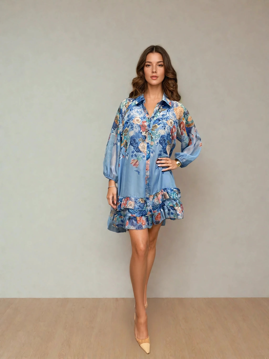 Woman wearing a light blue floral button-down dress with long sleeves and a ruffled hem, standing against a neutral background with one hand on her hip