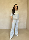 Model wearing a cream and beige jacquard knit two-piece set with subtle baroque print, standing against a textured beige wall.