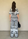 Back view of a woman wearing a black and white patterned knit matching set with a short-sleeve top and wide-leg pants, carrying a black faux fur handbag.