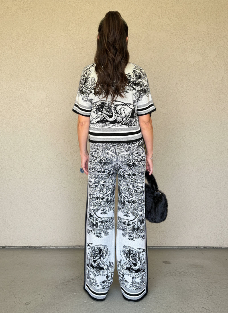 Back view of a woman wearing a black and white patterned knit matching set with a short-sleeve top and wide-leg pants, carrying a black faux fur handbag.