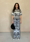 Front view of a woman wearing a black and white printed knit matching set, accessorized with a black faux fur handbag and white pointed-toe heels.