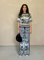 Front view of a woman wearing a black and white printed knit matching set, accessorized with a black faux fur handbag and white pointed-toe heels.