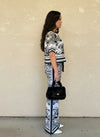 Side view of a woman dressed in a monochrome toile knit two-piece set, accessorized with a black faux fur handbag and white pointed heels.