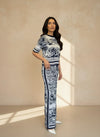 Woman wearing a navy and white jacquard knit top and matching wide-leg pants with a toile de Jouy print, standing against a beige wall in natural light.