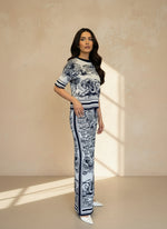 Woman wearing a navy and white jacquard knit top and matching wide-leg pants with a toile de Jouy print, standing against a beige wall in natural light.