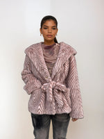 Fashion model showcasing a light pink chevron faux fur coat with hood and tie belt, styled with ripped jeans and neutral mesh top.
