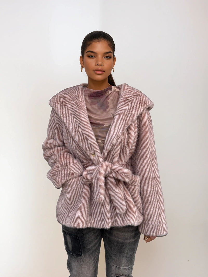 Fashion model showcasing a light pink chevron faux fur coat with hood and tie belt, styled with ripped jeans and neutral mesh top.