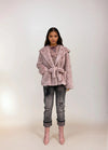 Full-length photo of model wearing a pink chevron faux fur coat with belt, distressed cuffed jeans, and shiny pink ankle boots.