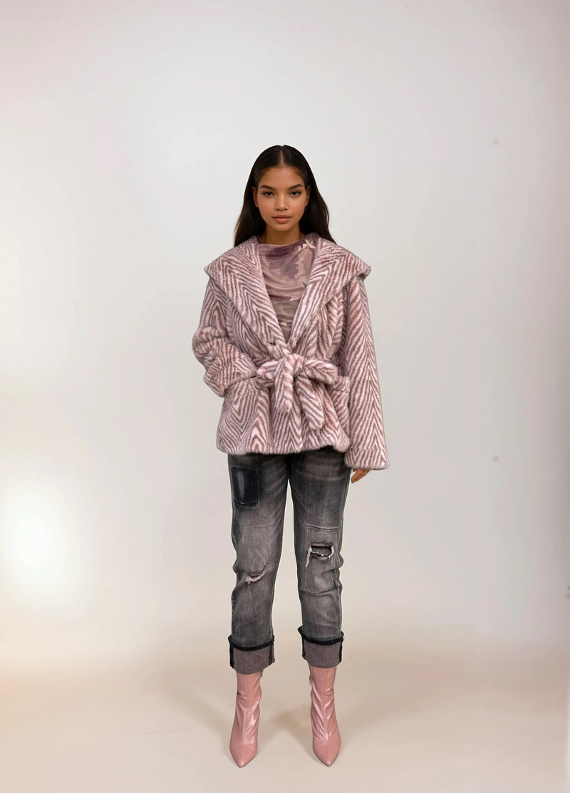 Full-length photo of model wearing a pink chevron faux fur coat with belt, distressed cuffed jeans, and shiny pink ankle boots.