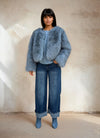Full-body view of a woman wearing a light blue faux fur jacket with wide-leg denim jeans and blue boots.