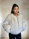 Woman dressed in a soft white faux fur jacket with subtle grey accents, standing in front of a minimalist beige background. Her dark hair is styled in a high ponytail, creating a clean, modern, and sophisticated winter outfit aesthetic.