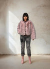 Model wearing a soft pink faux fur jacket with distressed gray jeans and pink boots in a neutral studio background.