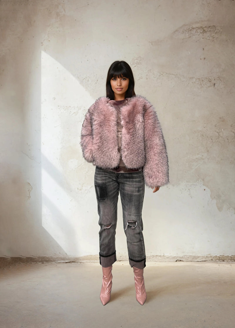 Model wearing a soft pink faux fur jacket with distressed gray jeans and pink boots in a neutral studio background.
