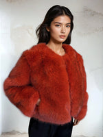 Elegant woman wearing a bold orange faux fur jacket paired with black trousers in a modern indoor setting.