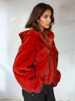 Side profile of model in a vibrant red faux fur cropped jacket with a hood and front flap pockets, paired with black jeans.