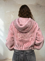 Back view of pink faux fur hooded jacket featuring embroidered “amore” text on the back, worn with faded grey jeans.