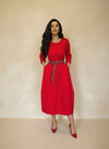 Front view of a model wearing a red belted midi dress with pockets and red pumps, styled for a sophisticated modern look.