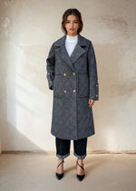 Model in a black gray double-breasted checkered wool coat with gold buttons, styled with rolled-up jeans and black pointed heels for minimalist winter fashion