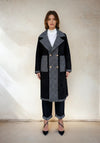Model showcasing a black and gray contrast double-breasted coat with oversized lapels and gold buttons, styled with cuffed denim and black heels
