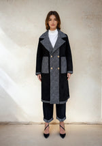 Model showcasing a black and gray contrast double-breasted coat with oversized lapels and gold buttons, styled with cuffed denim and black heels