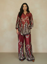 Woman modeling a rich burgundy silk baroque print ensemble with long-sleeve button-down top and matching flowy pants. Luxe coordinated outfit perfect for evening or resort style.