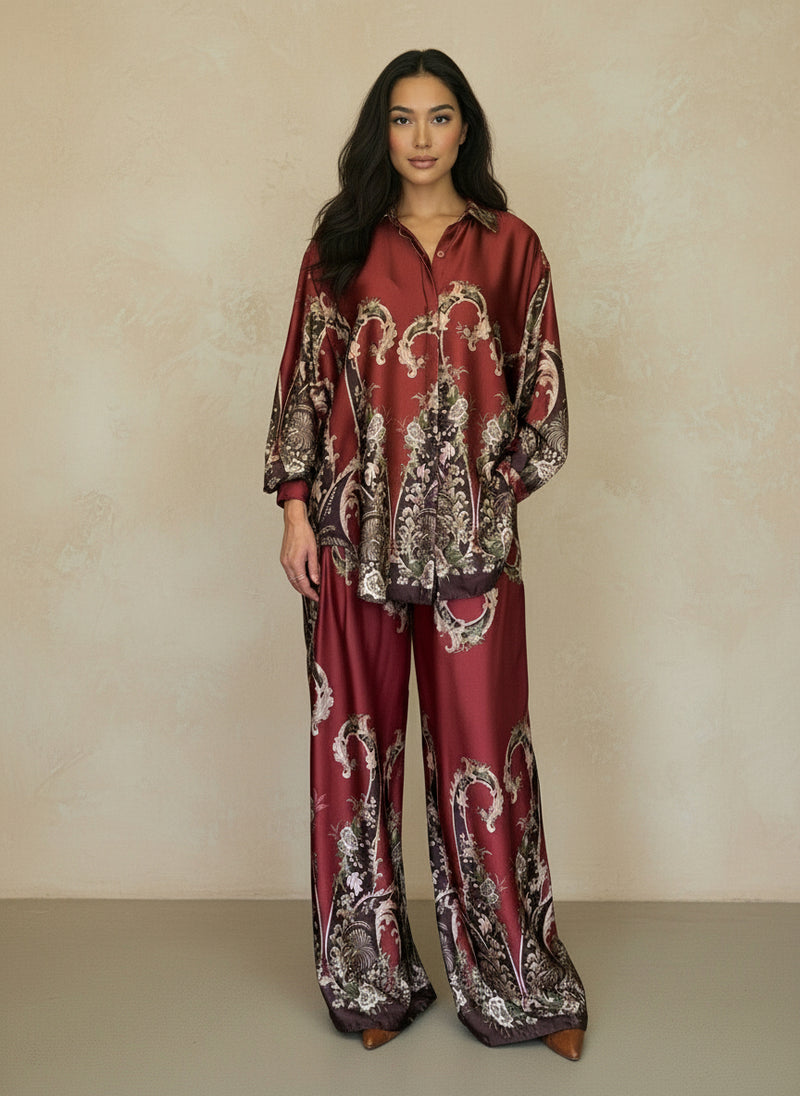 Woman modeling a rich burgundy silk baroque print ensemble with long-sleeve button-down top and matching flowy pants. Luxe coordinated outfit perfect for evening or resort style.