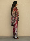 Side view of a woman in a burgundy silk two-piece set with ornate floral baroque patterns, wide-leg trousers, and oversized blouse. Elegant and comfortable fashion outfit.
