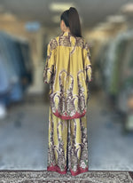Back view of a chartreuse silk baroque print co-ord set with maroon border details. Oversized shirt and matching wide-leg trousers in opulent design.