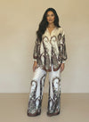 Model wearing a cream satin baroque print coordinated set featuring floral brown motifs and relaxed wide-leg pants. Elegant high-end women’s loungewear look.