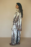 Side view of a model wearing an ivory silk co-ord set with ornate brown and green floral patterns. Elegant baroque-inspired two-piece outfit with flowy silhouette.