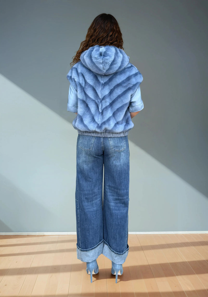 Back view of a woman modeling a blue faux fur sleeveless hoodie showing the chevron fur pattern and hood shape under natural light.