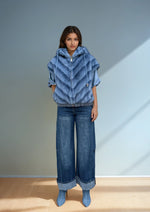 Full-body view of a model in a blue faux fur vest with hood and drawstrings, paired with wide-leg cuffed denim pants and heeled boots.