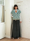 Full-length image of woman wearing a mint green faux fur vest with chevron texture and hood, paired with contrast black wide-leg pants and light heels, standing by a white brick wall.