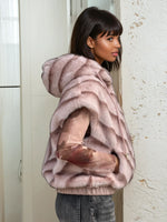 Back view of a woman modeling a blue faux fur sleeveless hoodie showing the chevron fur pattern and hood shape under natural light.