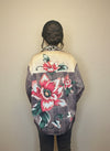 Back view of a plaid floral blouse featuring large red and pink flower prints and leopard collar detail, worn by a model with her hair in a bun inside a clothing boutique.