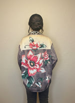 Back view of a plaid floral blouse featuring large red and pink flower prints and leopard collar detail, worn by a model with her hair in a bun inside a clothing boutique.