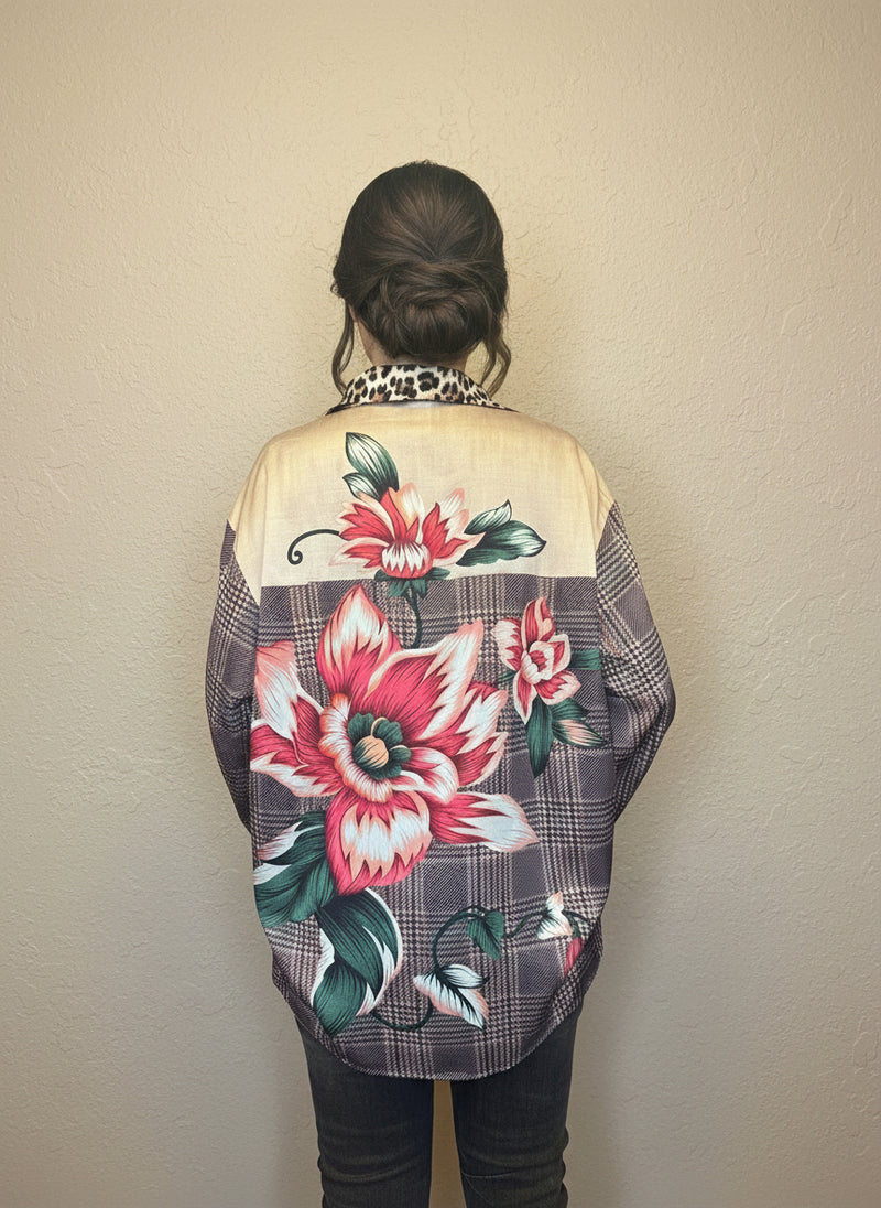 Back view of a plaid floral blouse featuring large red and pink flower prints and leopard collar detail, worn by a model with her hair in a bun inside a clothing boutique.